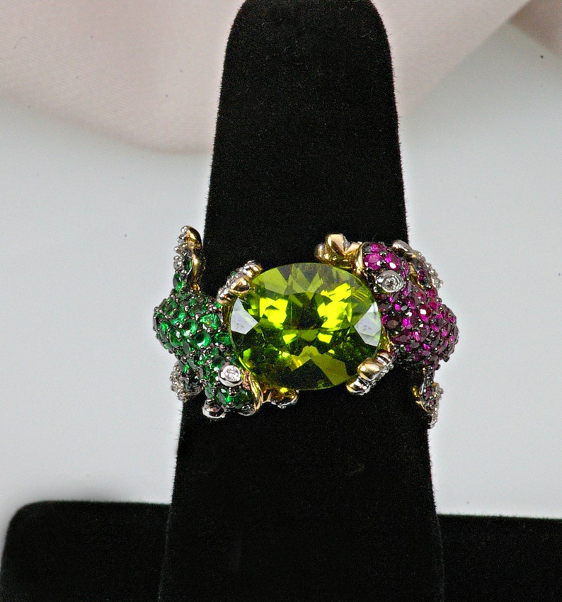 May include: A gold ring with a large green gemstone surrounded by smaller green, pink, and white gemstones.