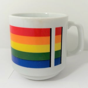 May include: White ceramic mug with a rainbow design. The rainbow is made up of red, orange, yellow, green, blue, and purple stripes.