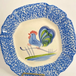 Puede incluir: Un plato de cerámica azul y blanco con un diseño de gallo. El plato tiene un borde festoneado y un esmalte azul moteado.