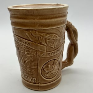 May include: A brown ceramic mug with a raised design of a bird and the words "Badlands National Park" and "VAMPIRE SANDS". The mug has a twisted handle.