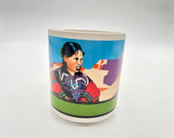 Może przedstawiać: Biały kubek ceramiczny z kolorową ilustracją kobiety w tradycyjnym stroju na niebieskim i fioletowym tle. Kobieta ma na sobie czerwoną i fioletową sukienkę z turkusową biżuterią.
