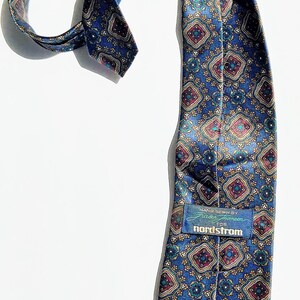 May include: A patterned blue tie with a repeating geometric design in red, gold, and teal. The tie has a red lining and a tag that reads "nordstrom".