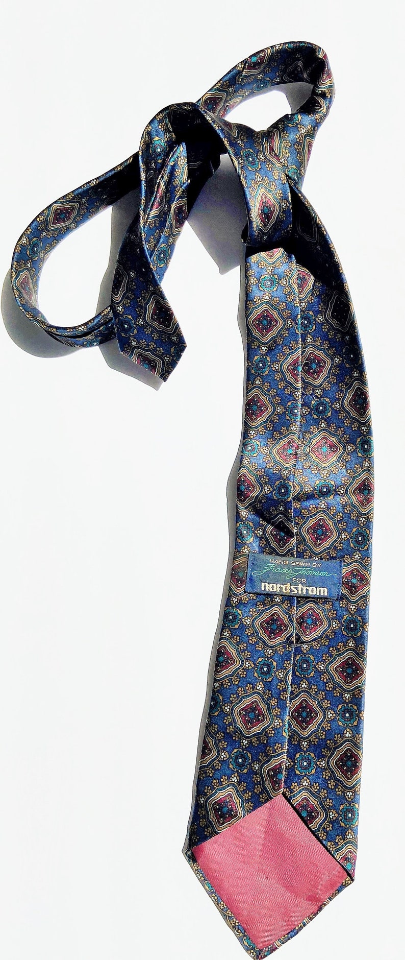 May include: A patterned blue tie with a repeating geometric design in red, gold, and teal. The tie has a red lining and a tag that reads "nordstrom".