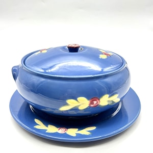 May include: A blue ceramic soup tureen with a lid and a matching saucer. The tureen and saucer are decorated with yellow leaves and red roses.