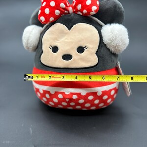 Puede incluir: Un juguete de peluche rojo y blanco con lunares, con una cara negra y un lazo rojo. El juguete tiene orejeras blancas y mide aproximadamente 15 cm de alto.