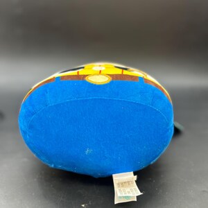 May include: Blue plush toy with a yellow and brown design. The toy is shaped like a character with a round head and a body. The toy has a tag on the bottom that says "Disney Pixar Toy Story".