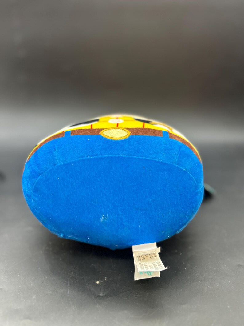 May include: Blue plush toy with a yellow and brown design. The toy is shaped like a character with a round head and a body. The toy has a tag on the bottom that says "Disney Pixar Toy Story".