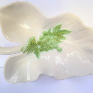 May include: A white ceramic leaf-shaped serving dish with a green grape design. The dish is ideal for serving snacks or appetizers.
