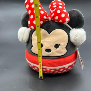 Puede incluir: Un juguete de peluche de Minnie Mouse, la novia de Mickey Mouse. Lleva un vestido rojo con lunares blancos, un lazo rojo y orejeras blancas. El juguete mide aproximadamente 18 cm de alto.