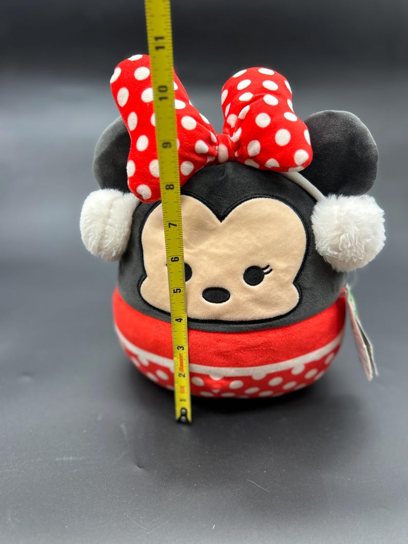 Puede incluir: Un juguete de peluche de Minnie Mouse, la novia de Mickey Mouse. Lleva un vestido rojo con lunares blancos, un lazo rojo y orejeras blancas. El juguete mide aproximadamente 18 cm de alto.