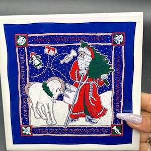 Puede incluir: Azulejo de cerámica cuadrado con temática navideña con borde azul. La imagen presenta a Papá Noel con abrigo rojo, un unicornio blanco y el texto "Making Merry, Making Magic" y "A Time of Good Cheer and Giving."