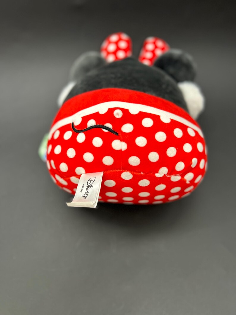 Puede incluir: Un juguete de peluche rojo y blanco con lunares, con una cara y orejas negras. El juguete tiene una etiqueta blanca que dice "Disney".
