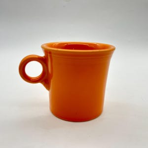 May include: A bright orange ceramic mug with a rounded handle. The mug is a classic style with a simple design.