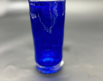 Peut inclure: Un petit verre à liqueur en verre bleu cobalt. Le verre cylindrique a un sommet légèrement évasé et une base épaisse et transparente. Le verre est transparent, laissant passer la lumière, et a une finition lisse et brillante.