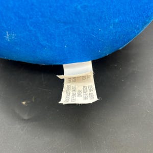 May include: A blue fabric tag with white text that reads "BAUX NEUSSRULERENT NEW M DE PERMIS:1740-2593 REG.N FBRES DE POLYESTER POLY FEUTRE DE POLYESTER POL"