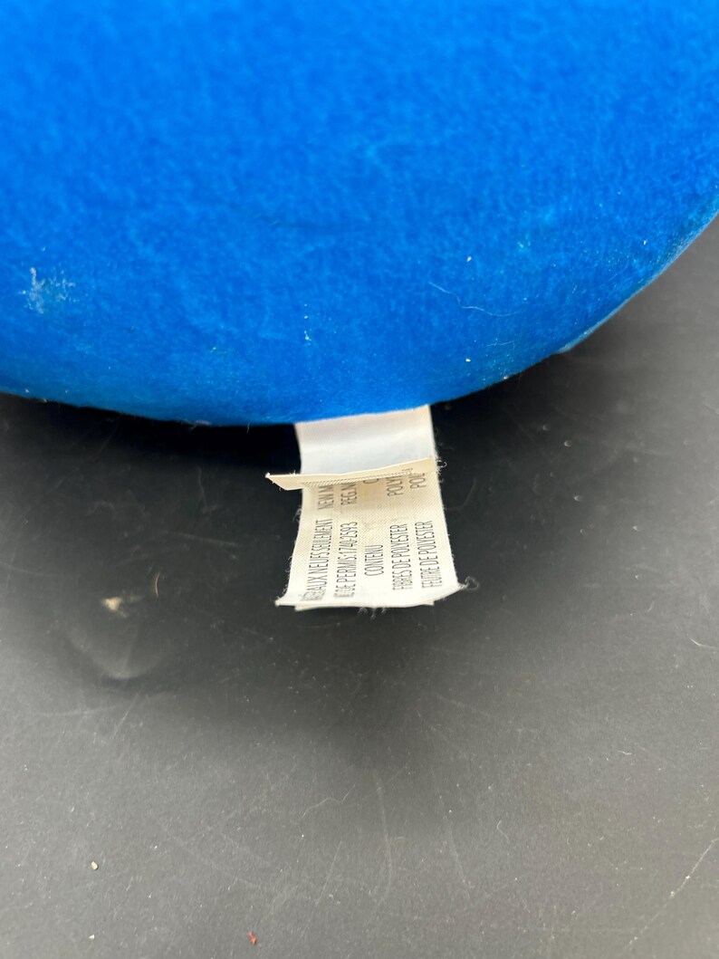 May include: A blue fabric tag with white text that reads "BAUX NEUSSRULERENT NEW M DE PERMIS:1740-2593 REG.N FBRES DE POLYESTER POLY FEUTRE DE POLYESTER POL"