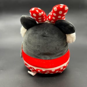 Puede incluir: Un juguete de peluche con forma de rat&oacute;n de dibujos animados con un lazo rojo con lunares blancos. El rat&oacute;n lleva una falda roja y blanca con lunares blancos. El juguete es negro, rojo y blanco.