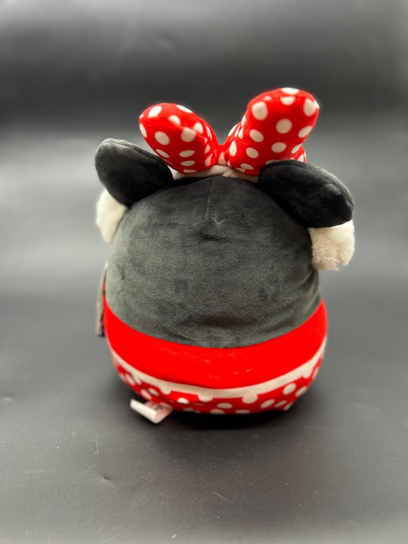 Puede incluir: Un juguete de peluche con forma de rat&oacute;n de dibujos animados con un lazo rojo con lunares blancos. El rat&oacute;n lleva una falda roja y blanca con lunares blancos. El juguete es negro, rojo y blanco.