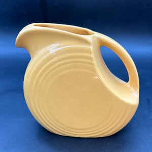 May include: A yellow ceramic pitcher with a rounded, wave-like design. The pitcher has a wide mouth and a handle.