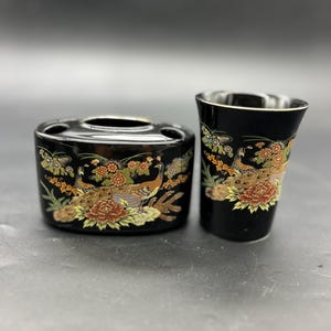 May include: Black and gold ceramic toothbrush holder and tumbler set with a floral and peacock design.