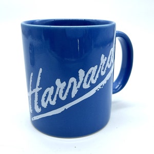 May include: A blue ceramic mug with a white inscription that reads "Harvard" in a slanted, handwritten font.