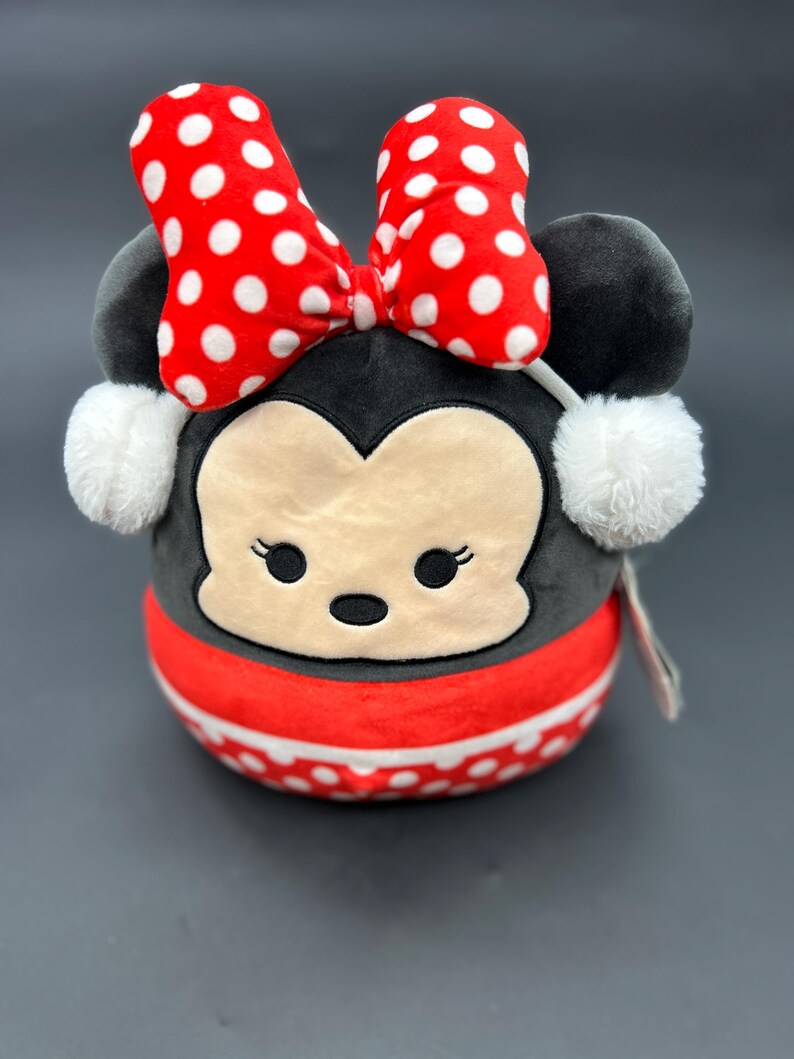 Puede incluir: Un juguete de peluche con forma de rat&oacute;n de dibujos animados con un lazo rojo y lunares blancos. El rat&oacute;n lleva una bufanda de rayas rojas y blancas y tiene orejeras de piel blanca.