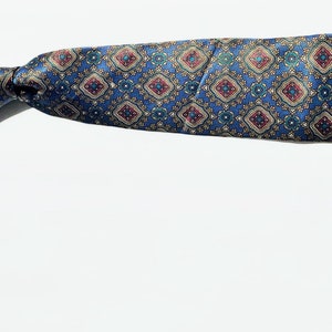 May include: A patterned necktie with a blue background and a repeating diamond design in red, gold, and green. The tie is knotted and lies on a white surface, showcasing its intricate pattern and color scheme.