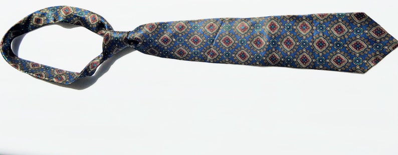 May include: A patterned necktie with a blue background and a repeating diamond design in red, gold, and green. The tie is knotted and lies on a white surface, showcasing its intricate pattern and color scheme.