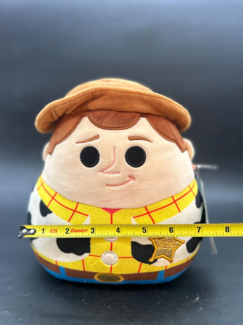 May include: A plush toy of Woody from Toy Story. He is wearing his signature cowboy hat, vest, and sheriff's badge. The toy is approximately 18 cm tall.