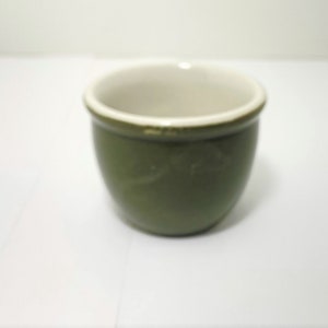 Może przedstawiać: Mały, zielony kubek ceramiczny z białym wnętrzem. Kubek jest okrągły i ma gładkie, błyszczące wykończenie.