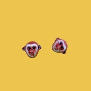 May include: A pair of monkey face earrings. The earrings are made of ceramic and are painted in shades of brown and white.