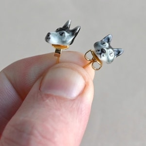 May include: A pair of gold stud earrings featuring a black and white porcelain husky dog head design.