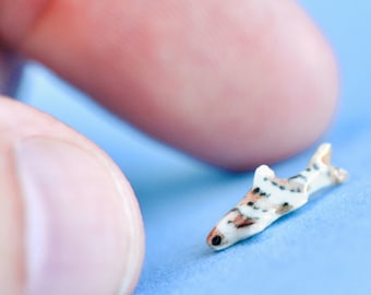 May include: A small, white and brown ceramic figurine of a shark. The figurine is about the size of a fingernail.