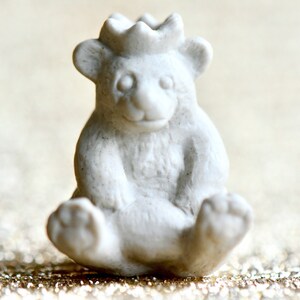May include: White ceramic figurine of a bear wearing a crown. The bear is sitting with its paws tucked in front of it. The figurine is a whimsical and charming addition to any home decor.