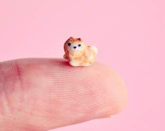 May include: A small, ceramic figurine of a brown and white dog sitting on a finger. The dog has black eyes and a brown nose.