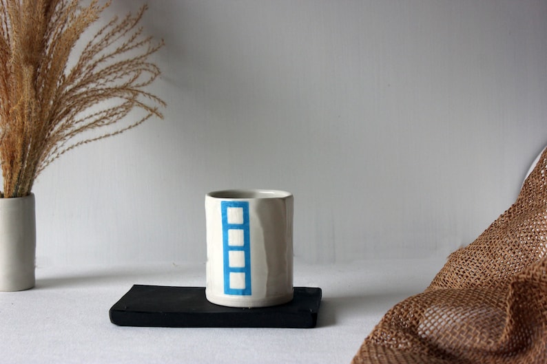 May include: White ceramic mug with a blue geometric design. The mug is sitting on a black rectangular tray.