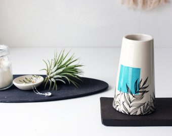 May include: White ceramic vase with a blue and black geometric design. The vase is decorated with black line drawings of leaves and branches.