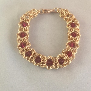 Könnte beinhalten: Ein goldenes Kettenarmband mit roten Kristallperlen. Das Armband hat einen Karabinerverschluss.