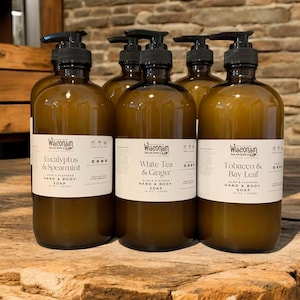 May include: Four amber glass bottles of hand and body soap with pump tops. The bottles are labeled with the brand name "Wisconsin" and the scents "Eucalyptus & Spearmint", "White Tea & Ginger", and "Tobacco & Bay Leaf".