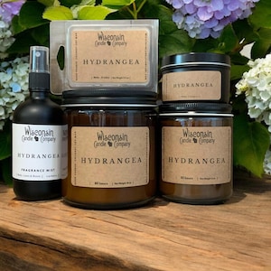 May include: A set of hydrangea-scented candles and a fragrance mist. The candles are in amber glass jars with brown labels that read "Wisconsin Candle Company" and "Hydrangea". The fragrance mist is in a black bottle with a white label that reads "Wisconsin Candle Company" and "Hydrangea Fragrance Mist".