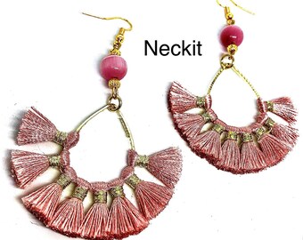 May include: A pair of pink tassel earrings with gold accents and a pink bead. The earrings are shaped like a crescent moon and have a dangling design. The text "Neckit" is visible in the image.