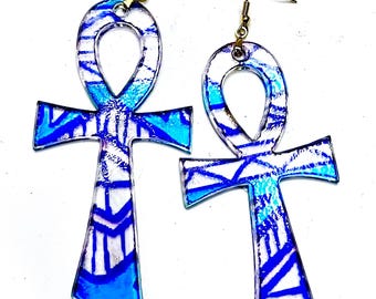 May include: A pair of Ankh-shaped earrings with a blue and white geometric pattern. The earrings have gold-colored hooks and the word "Neckit" is printed at the bottom.