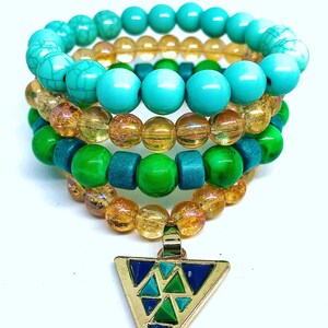 May include: A multi-layered necklace with turquoise, green, and gold beads. The necklace has a triangular pendant with a geometric pattern in shades of blue, green, and turquoise.