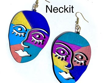 May include: A pair of drop earrings featuring abstract face designs with color-blocked sections in blue, yellow, teal, purple, and coral. The faces have white cut-out details for eyes and lips. The word Neckit is printed in black near the top.