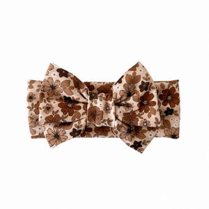 May include: A floral headband with a large bow. The headband and bow feature a pattern of small flowers in shades of brown, tan, and white, set against a tan background.