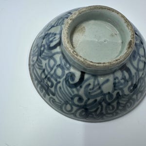 May include: An antique ceramic bowl with a blue and white swirling pattern. The bowl's exterior features a detailed, ornate design, while the interior and base are a solid light blue. The bowl is likely vintage and shows signs of age.