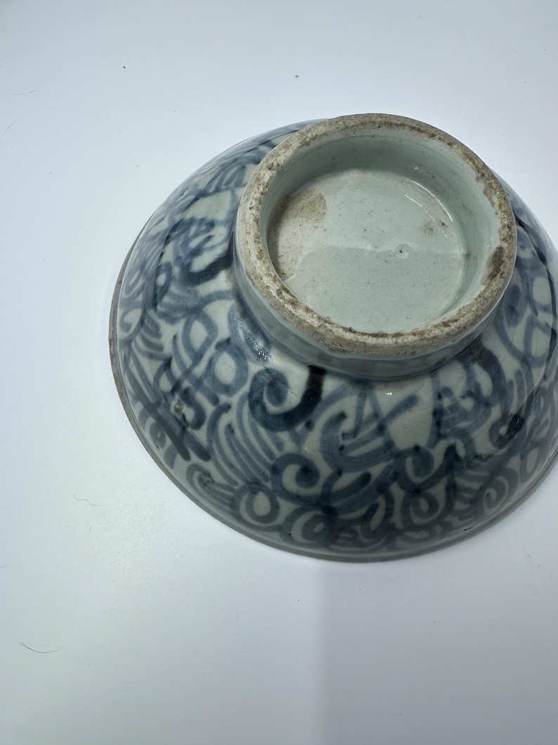 May include: An antique ceramic bowl with a blue and white swirling pattern. The bowl's exterior features a detailed, ornate design, while the interior and base are a solid light blue. The bowl is likely vintage and shows signs of age.