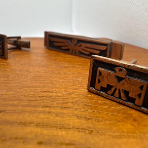 Pode incluir: Uma caneca de cerâmica branca com uma alça preta e o texto "But First, Coffee" em negrito preto. A caneca está sobre um fundo desfocado. A caneca tem aproximadamente 10 cm de altura.