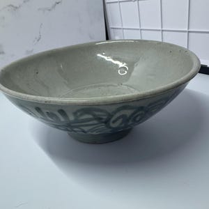 May include: A light gray ceramic bowl with a slightly angled rim. The bowl has a footed base and is decorated with a blue, swirling pattern around the exterior. The bowl is likely used for serving food.