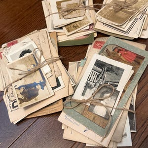 May include: A collection of vintage photographs and postcards bundled into four separate stacks, each tied with thin brown twine. The stacks contain various black-and-white and sepia-toned images, including portraits, landscapes, and handwritten notes.